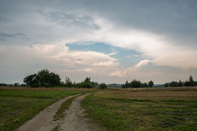 Dirt road amidst field against sky