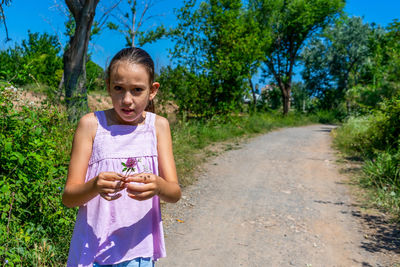 Portrait of girl holding flower standing on footpath