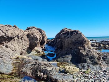 Rock formations in sea against clear blue sky