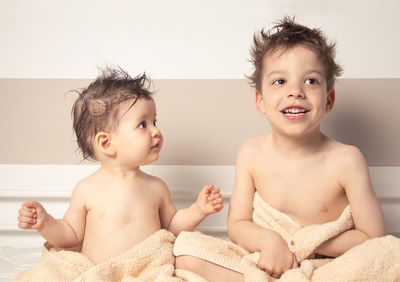 Cute shirtless siblings wrapped in towel against wall