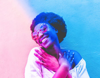 Smiling young woman in sunglasses against wall