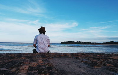 Rear view of man sitting by sea against sky