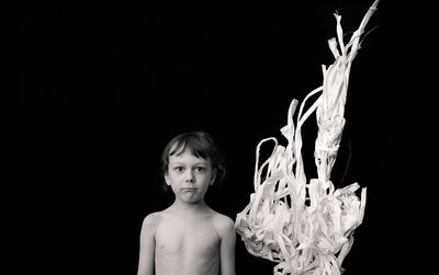 Portrait of shirtless boy standing against black background