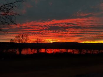 Silhouette trees by lake against romantic sky at sunset