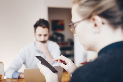 Woman using mobile phone against man working on laptop at home