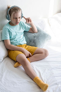 Cute boy listening to music in earphones seating on bed. child wearing headphones listens to music.