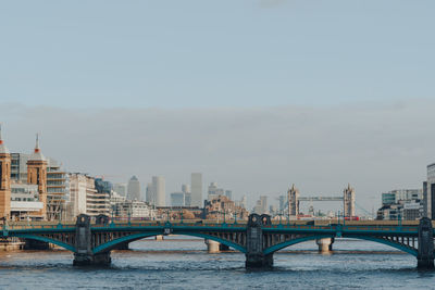 Bridge over river by buildings against sky