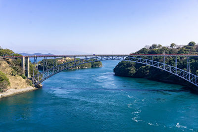 Bridge over calm river against clear blue sky