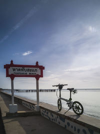 Information sign by sea against sky