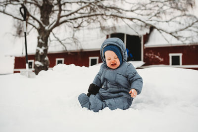 Baby crying sitting on snow in norway with red barn behind
