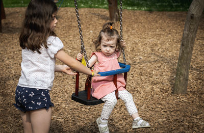 Portrait of a girl pushing her younger sister on a swing.