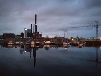 Factory by river against sky in city