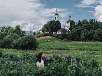 Rear view of woman sitting on grassy field against sky