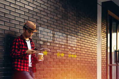 Young man holding coffee cup standing against wall