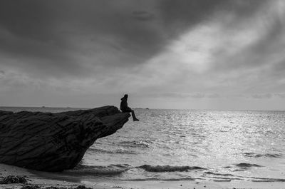 Man sitting on rock over sea against sky