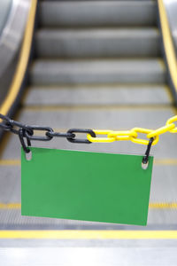 Close-up of green blank placard attached to chain against escalator