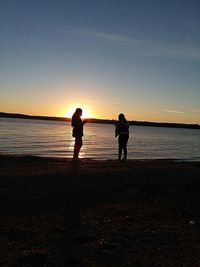 Silhouette men standing on beach against sky during sunset