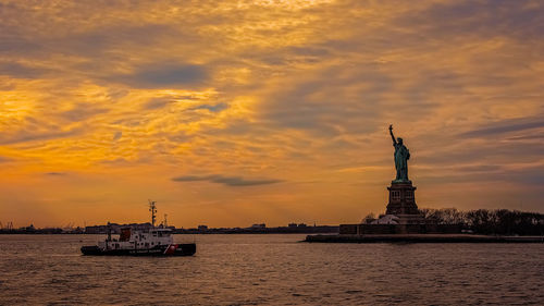 Statue of liberty against cloudy sky during sunset