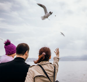 Rear view of man with seagulls flying over sea against sky