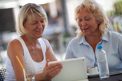 Mature woman showing digital tablet to friend at sidewalk cafe