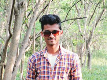 Portrait of happy young man standing by tree in forest