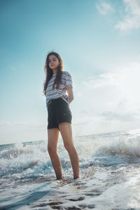 Young woman standing on beach against sky