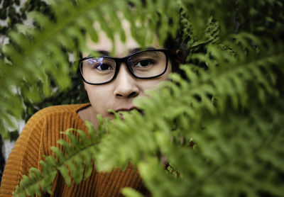 Close-up portrait of young woman wearing eyeglasses seen through leaves