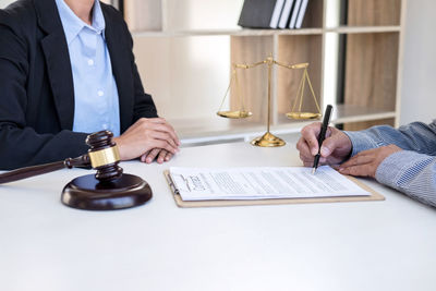 Cropped image of man signing on paper with lawyer in courtroom