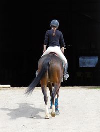 Rear view of woman horseback riding on field