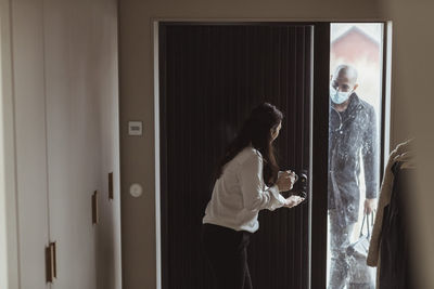 Side view of woman standing by window at home