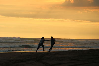 Men on beach against sky during sunset