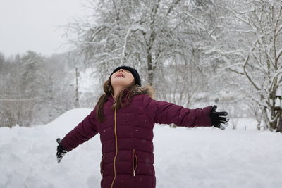 Girl with arms outstretched standing on snow against bare trees