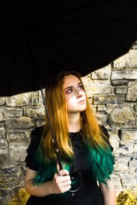 Young woman holding camera while standing against brick wall