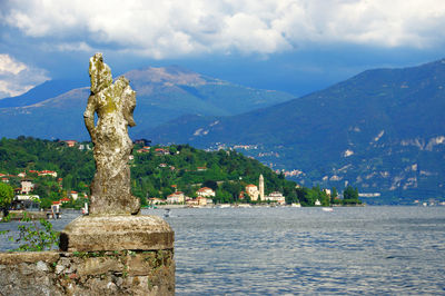 Old ruin statue on retaining wall at lake como against cloudy sky