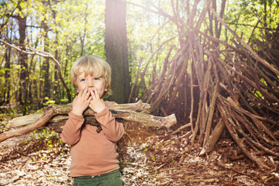 Portrait of young woman standing amidst tree trunk