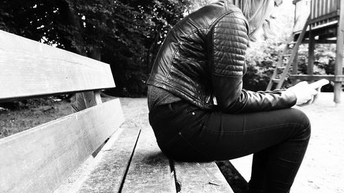 Side view of young woman using mobile phone while sitting on bench at park