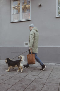 Full length side view of man walking with dog on footpath in city