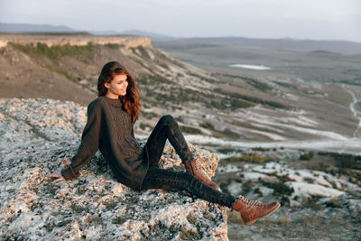 Side view of young woman sitting on rock