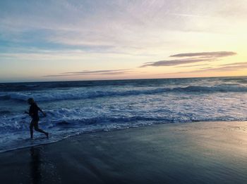 Side view of woman running on shore against sky during sunset 