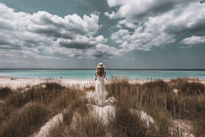 Rear view of woman standing at beach against sky