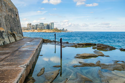 Scenic view of sea by city buildings against sky