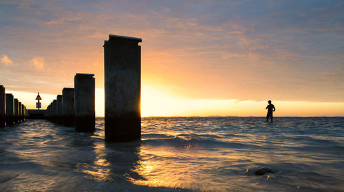 Silhouette man on wooden post by sea against sky during sunset
