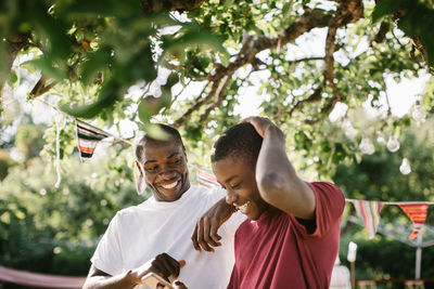 Happy father looking at son using mobile phone in backyard during garden party