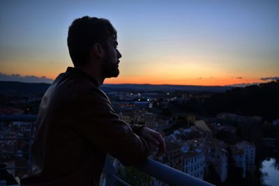 Man standing by cityscape against sky during sunset