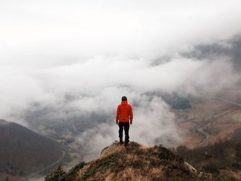 Rear view of man standing on mountain peak during foggy weather