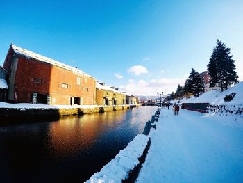 Snow covered canal by buildings against sky