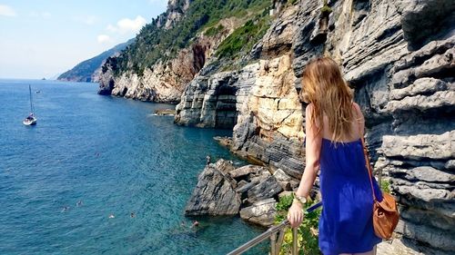 Rear view of woman standing at observation point by rocky coastline against sky