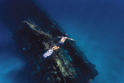 Man with arms outstretched swimming over shipwreck in sea