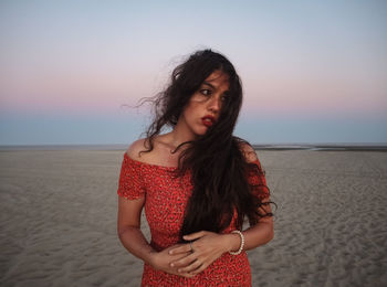 Young woman standing at beach against sky