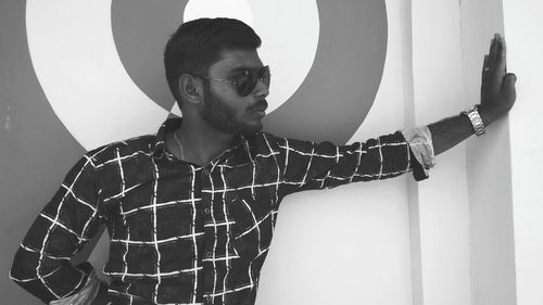 Young man wearing sunglasses standing against wall at home